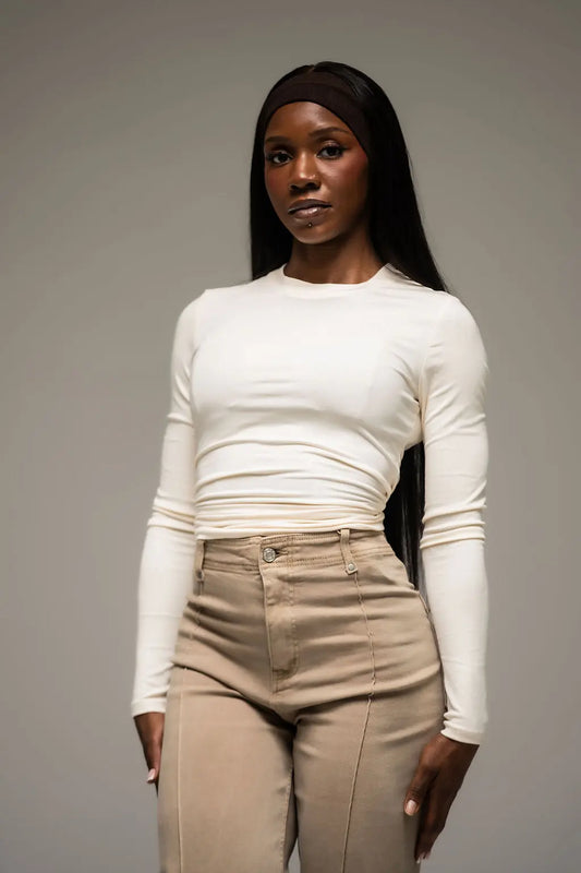Woman wearing a white long-sleeve top and beige pants against a gray background
