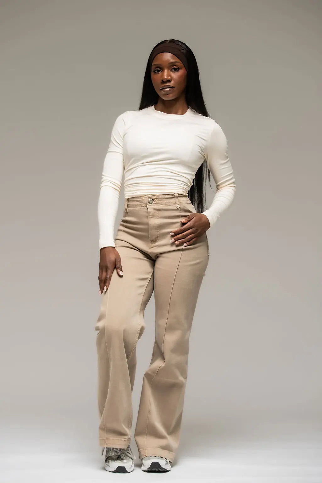 Woman wearing a white long-sleeve top and beige pants against a plain background